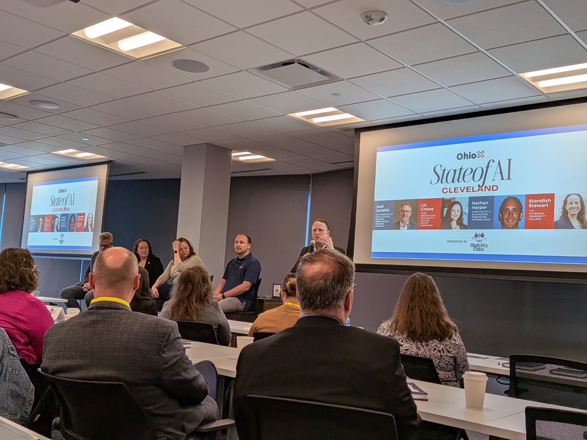 OhioX State of AI panelists sit at the front of a room at Park Place Technologies, with attendees seated at tables and event slides on two screens.